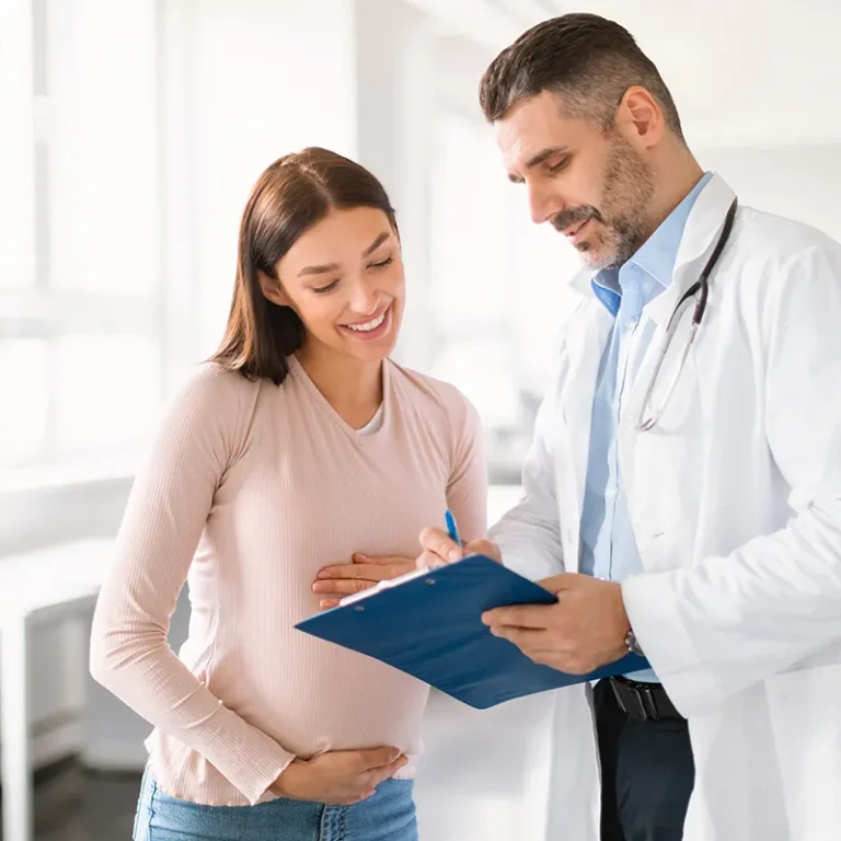 Médico especialista revisando el historial clínico con una mujer embarazada sonriente.
